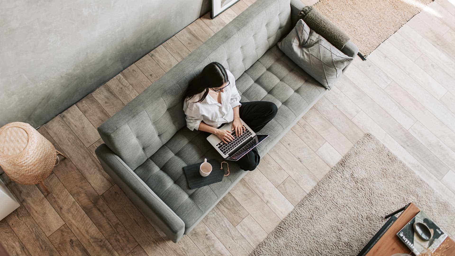 femme avec ordinateur portable sur sofa avec plancher de bois franc